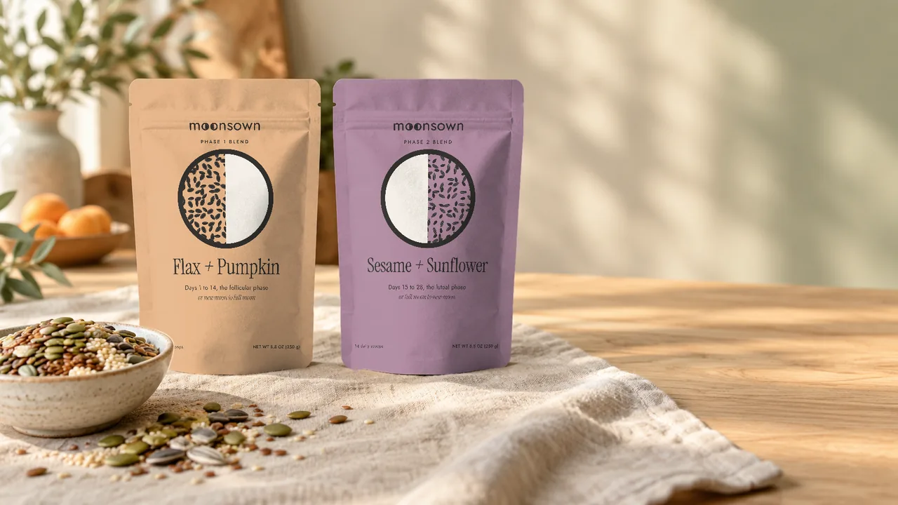 The Moonsown Phase 1 and Phase 2 Blend pouches on a linen cloth beside a bowl of mixed seeds